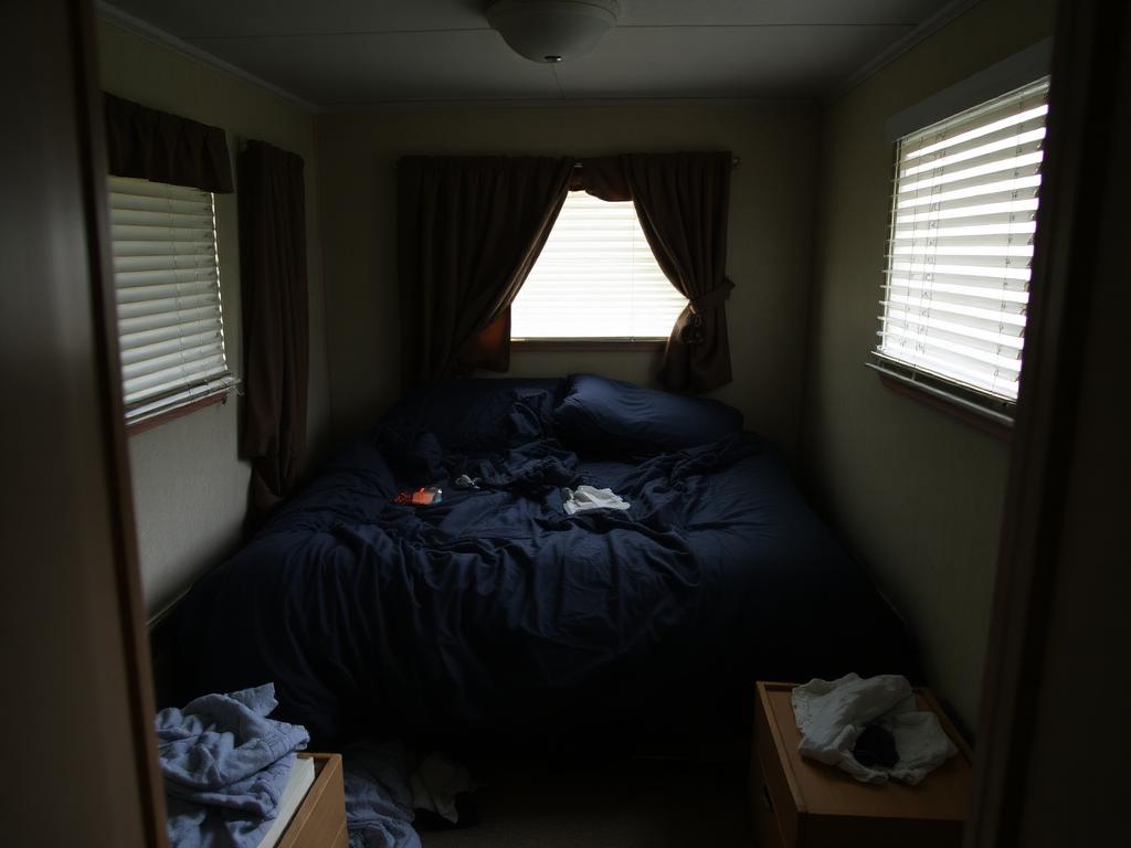 Dim, cluttered bedroom with unmade bed and personal items